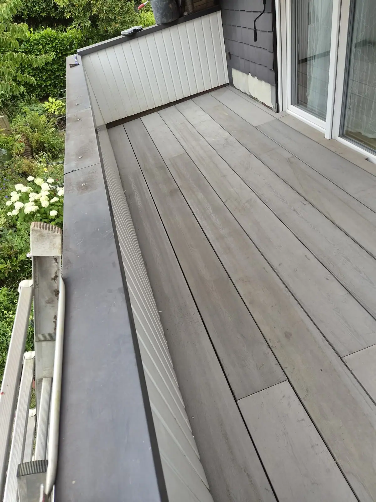 Balkon mit neu verlegten grauen Terrassendielen in Holzoptik, verkleideter Brüstung und Blick in den Garten
