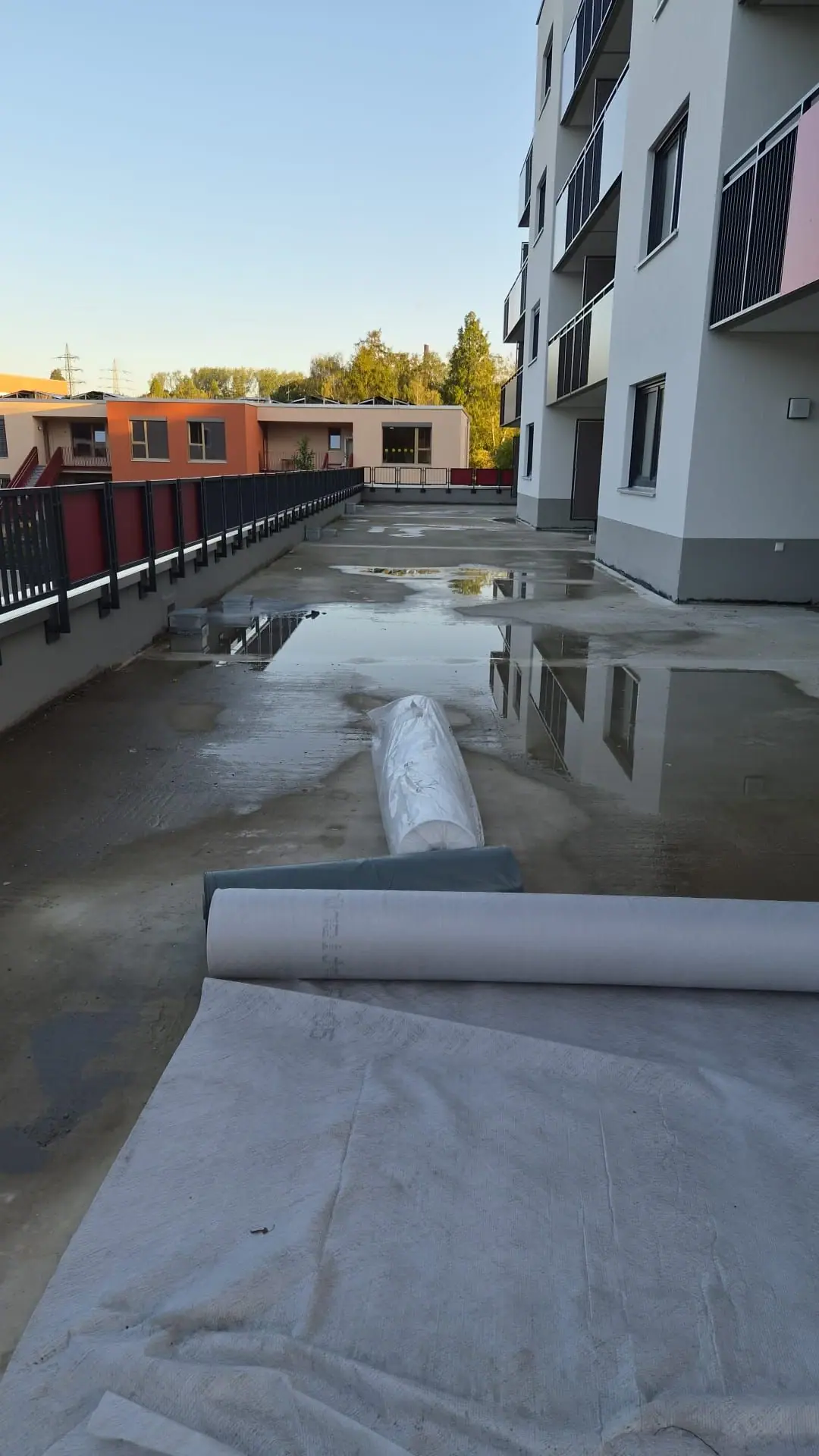 Nasse Betondecke vor einer neuen Wohnanlage mit ausgerollten Vliesbahnen vor Beginn des Gründachaufbaus