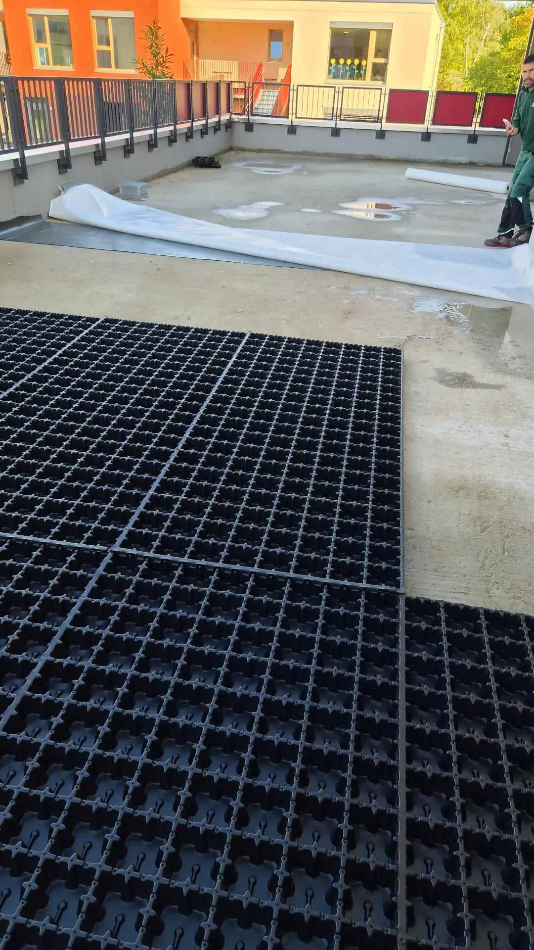 Verlegung schwarzer Dränelemente aus Kunststoff auf der Betondecke einer Wohnanlage, daneben Vliesbahnen