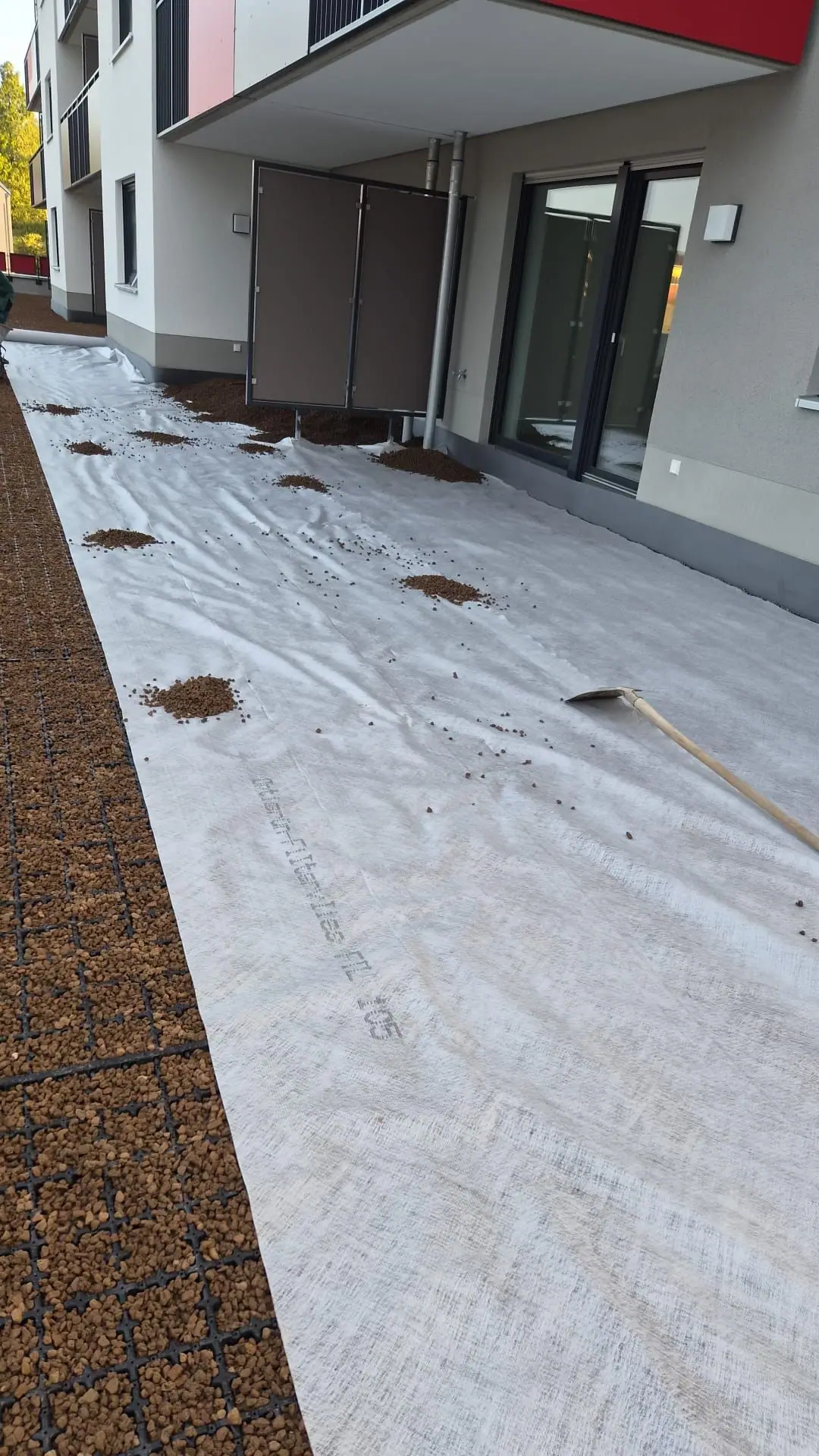 Filtervlies über der verfüllten Dränschicht mit ersten Häufchen Substrat vor den Terrassentüren einer Wohnanlage