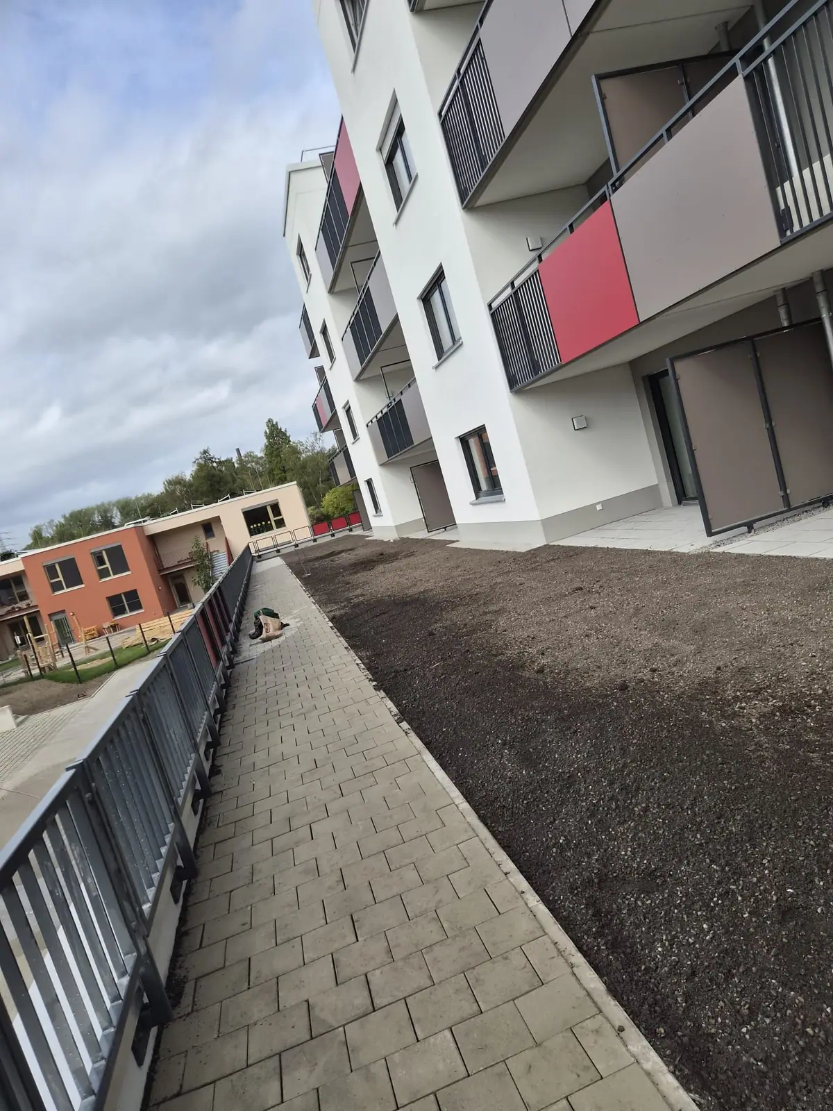 Fertiger Pflasterweg am Geländer und planierte Vegetationsfläche vor den Erdgeschosswohnungen einer neuen Wohnanlage
