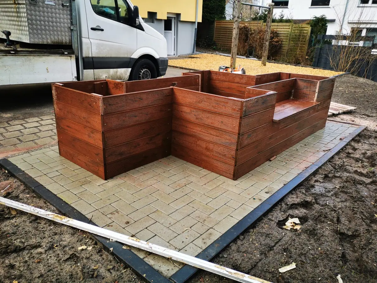 Hochbeet mit Sitzbank aus Holz auf einer gepflasterten Fläche während des Aufbaus