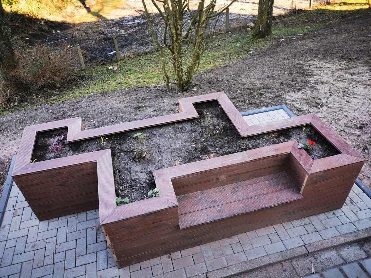 Bepflanztes Hochbeet aus Holz mit integrierter Sitzbank auf einer gepflasterten Fläche