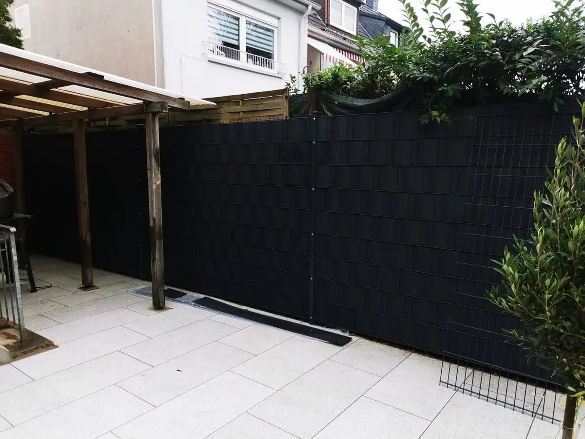 Sichtschutzzaun in Anthrazit neben einer Terrasse aus hellen Platten
