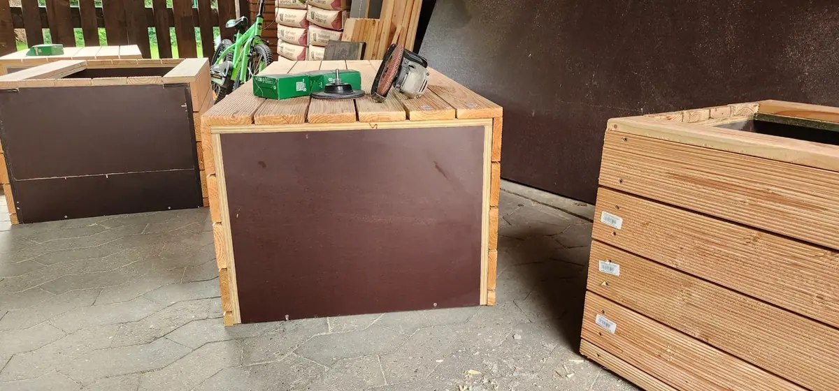 Vorgefertigte Holzmodule für eine Sitzbank mit Pflanzkästen, mit dunklen Innenplatten, daneben Werkzeug