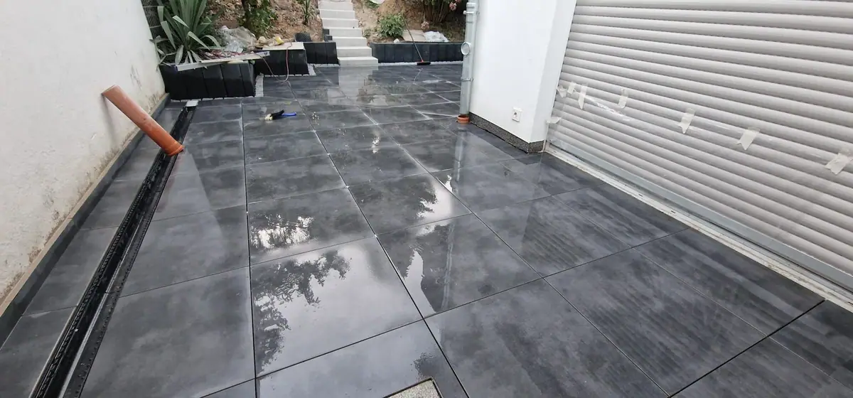 Terrasse aus anthrazitfarbenen Großformatplatten mit Schlitzrinne vor einer Garage