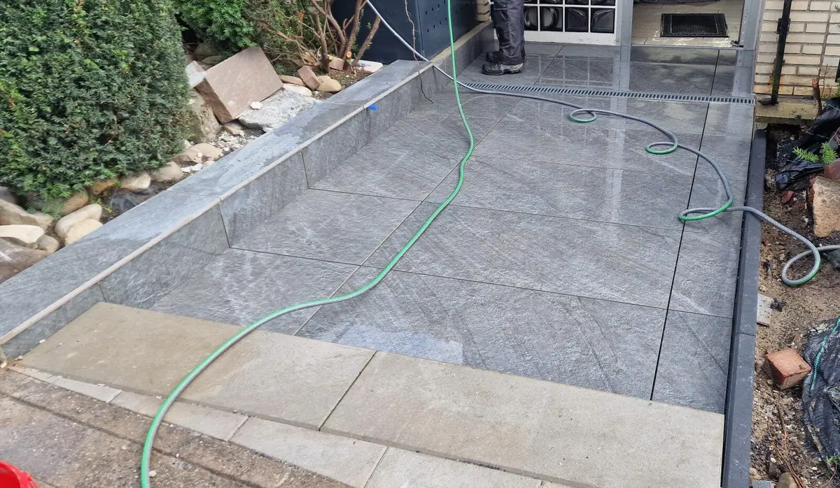 Terrasse aus grauen Feinsteinzeugplatten mit Entwässerungsrinne und Einfassung