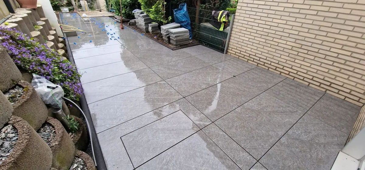 Großzügige Terrasse aus grauem Feinsteinzeug in Steinoptik neben einer hellen Klinkerwand