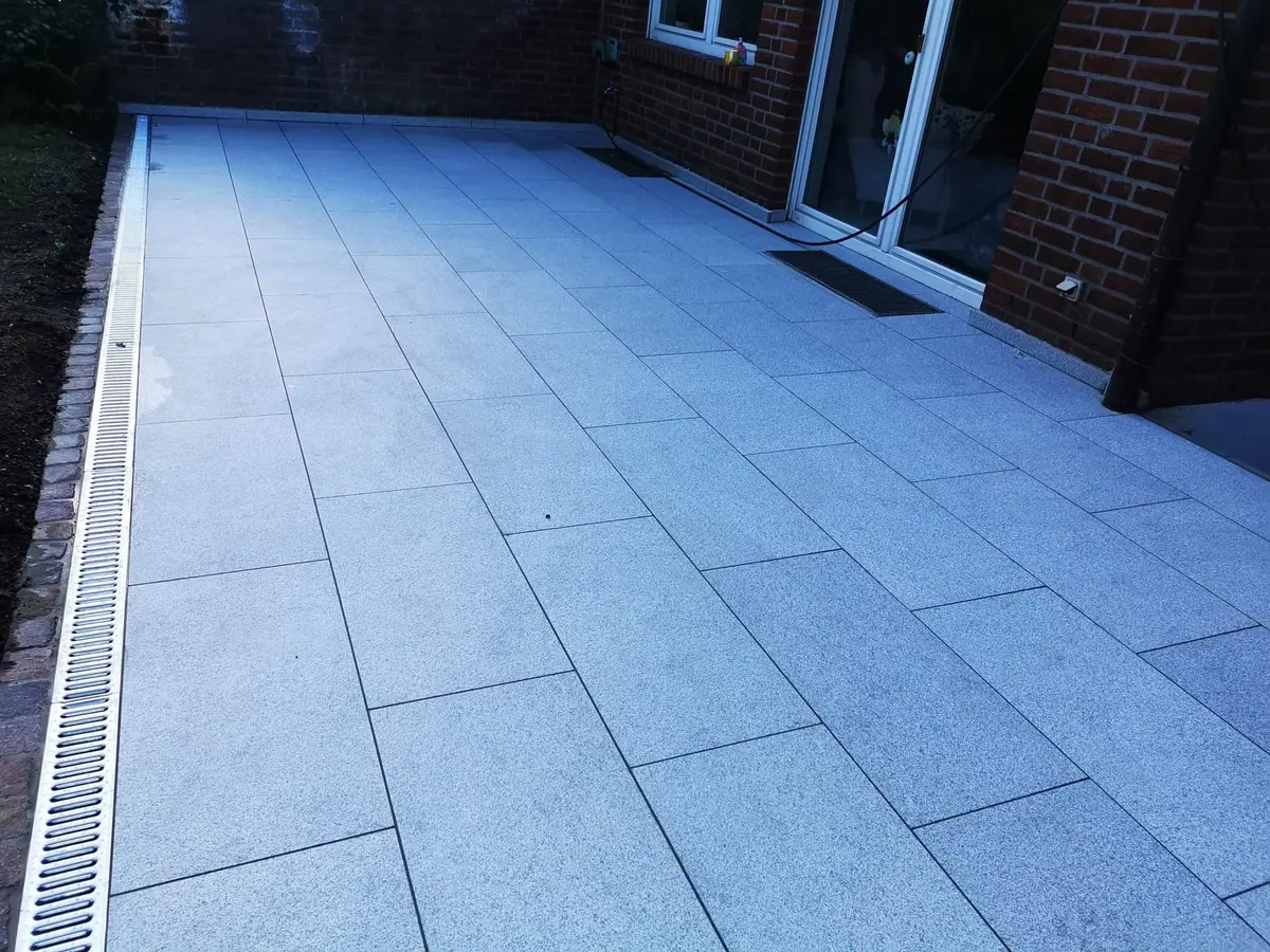 Terrasse aus hellen, großformatigen Granitplatten mit Entwässerungsrinne an einem Klinkerhaus