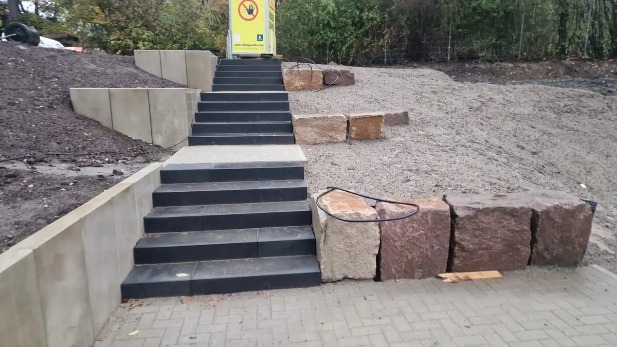 Treppenanlage aus anthrazitfarbenen Blockstufen mit Winkelstützmauern und Natursteinblöcken